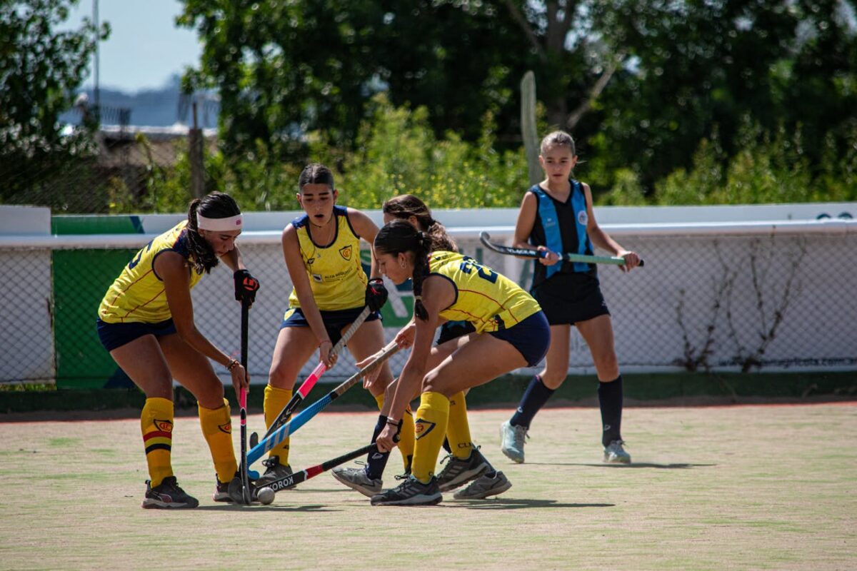 Young athletes competing in a dynamic field hockey game outdoors, showcasing teamwork and skill.