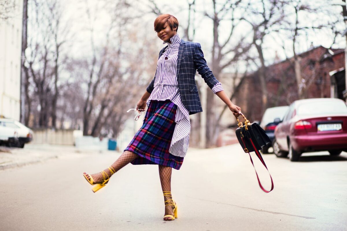 Fashionable woman striking a playful pose on a city street, showcasing vibrant style and joy.